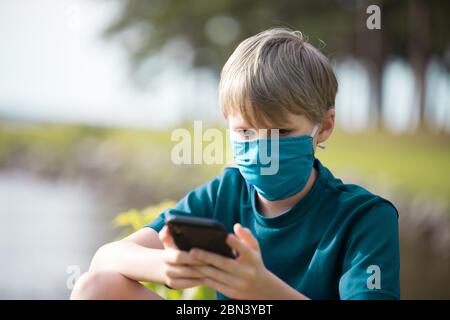 Person, die SMS auf dem Telefon während der grünen Gesichtsmaske zum Schutz während der Covid19-Pandemie trägt. Stockfoto