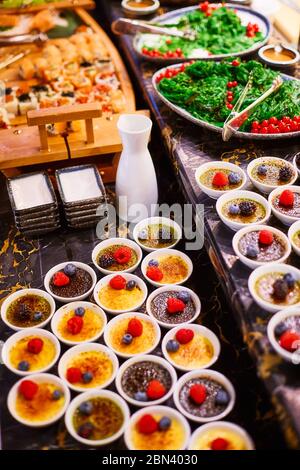 Ein Buffettisch, auf dem es zwei Arten von Soufflé in weißen Schalen gibt, die mit Himbeeren, Heidelbeeren und Brombeeren dekoriert sind Stockfoto