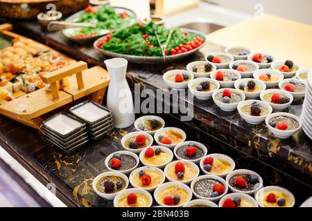 Ein Buffettisch, auf dem es zwei Arten von Soufflé in weißen Schalen gibt, die mit Himbeeren, Heidelbeeren und Brombeeren dekoriert sind Stockfoto