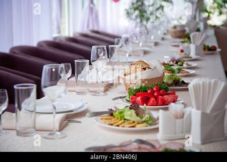 Ein Tisch mit einer weißen Tischdecke mit Salaten, Gläsern, Tellern, Servietten und einer Anzahl von Sitzplätzen bedeckt Stockfoto