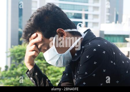 Ein junger Mann mit Schutzmaske hat Spannungskopfschmerzen. Stockfoto