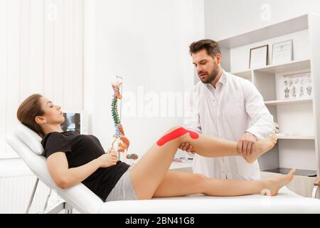 Kinesiologie Taping.Physikalischer Therapeut Anwendung von Kinesiologieband auf den Patienten Knie.Therapeut Behandlung verletzter Knie des jungen Athleten.Post traumatisch Stockfoto