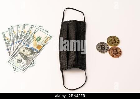 Schwarze medizinische Maske auf weißem Hintergrund Goldene Bitcoin-Münzen und US-Dollar aus nächster Nähe Stockfoto