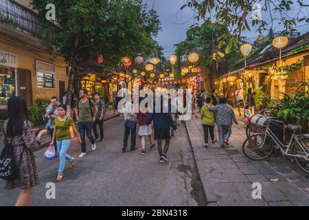 Wundervolle Aussicht auf die alte Straße, die mit bunten Seidenlaternen dekoriert ist. Vietnamesen in traditionellen schließt Spaziergang entlang Hoi an Altstadt. Hoi an (Hoi an), Vietnam - 12. März 2020. Stockfoto