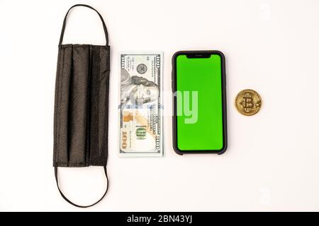Draufsicht einer schwarzen Schutzmaske, Dollarschein, Telefon mit grünem Bildschirm und Bitcoin Goldmünze auf weiß isoliert Stockfoto