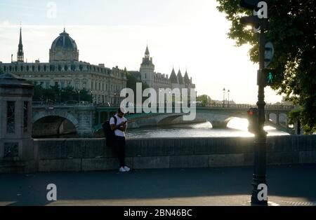 Ein Mann, der sein Handy mit der Brücke Pont d'Arcole über die seine betrachtet, im Hintergrund Greffe du Tribunal de Commerce de Paris und Conciergerie.Paris.Frankreich Stockfoto