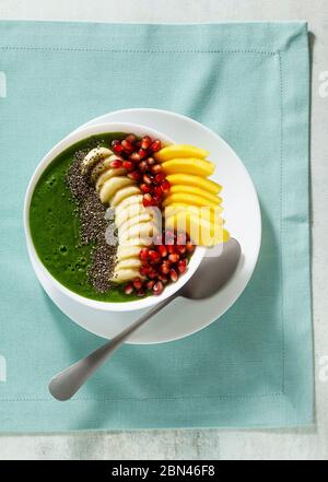 Schüssel mit grünem Smoothie mit geschnittenen Mango, Banane, Granatapfelkernen und Chiasamen, Ahornsirup für ein gesundes Frühstück am Morgen Stockfoto