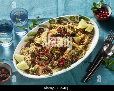 Couscous wird auf Orangensaft mit gekochtem Gemüse, karamellisierten Zwiebeln, Rosinen und Granatapfelkernen gekocht. Auf dem Tisch mit einer Leinentischdecke Stockfoto