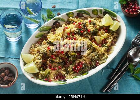 Couscous wird auf Orangensaft mit gekochtem Gemüse, karamellisierten Zwiebeln, Rosinen und Granatapfelkernen gekocht. Auf dem Tisch mit einer Leinentischdecke Stockfoto