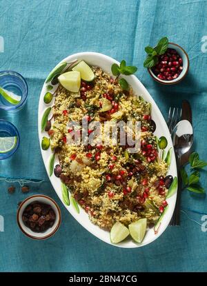 Couscous wird auf Orangensaft mit gekochtem Gemüse, karamellisierten Zwiebeln, Rosinen und Granatapfelkernen gekocht. Auf dem Tisch mit einer Leinentischdecke Stockfoto
