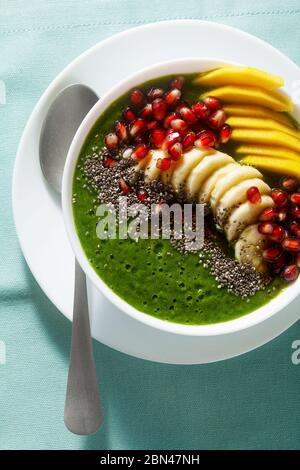 Schüssel mit grünem Smoothie mit geschnittenen Mango, Banane, Granatapfelkernen und Chiasamen, Ahornsirup für ein gesundes Frühstück am Morgen Stockfoto