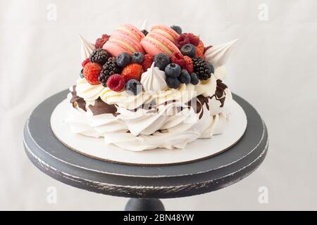 Pavlova Kuchen mit Schlagsahne, Himbeere, Heidelbeere, Brombeere und makronen. Kopierbereich, schlichter grauer Hintergrund. Stockfoto