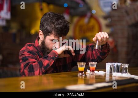 Get Drunk Concept. Hipster in der Nähe Gläser mit alkoholischem Getränk, kurzer Cocktail. Guy verbringen Freizeit in Bar trinken Cocktail, defokussed Hintergrund. Mann mit betrunkenem Gesicht sitzen alleine an der Theke. Stockfoto