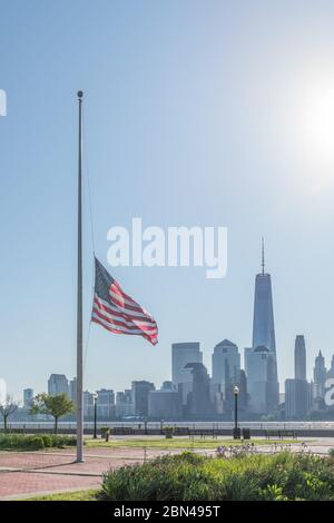Vertikal der Skyline von New York mit einer amerikanischen Flagge am halben Mast im Vordergrund von der anderen Seite des Hudson River. Stockfoto