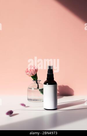 Glasflaschenspray mit Körperöl, Blumenwasser oder Gesichtstonikum. Schöne Vase mit einer Rose. Stockfoto