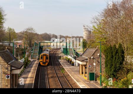 Ein Personenzug verlässt den Bahnhof von Chirk, im Hintergrund befindet sich ein Teil der Kronospan-Fabrik, North East Wales Stockfoto