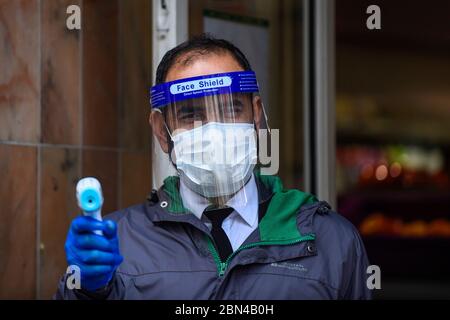 London, Großbritannien. 12 Mai 2020. Ein Wachmann mit Gesichtsschutz wartet darauf, die Temperaturkunden während der laufenden Sperrung der Coronavirus-Pandemie in einen Supermarkt in Chinatown zu überprüfen. Normalerweise sind die Straßen mit Touristen und Besuchern überfüllt, aber als Folge von Covid 19, wird der Fußabfall deutlich reduziert. Kredit: Stephen Chung / Alamy Live News Stockfoto