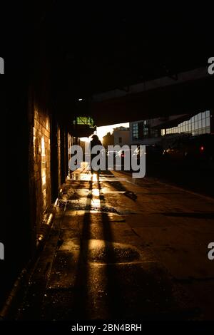 Eine anonyme Person wirft einen Schatten bei Sonnenuntergang unter einer Brücke Stockfoto