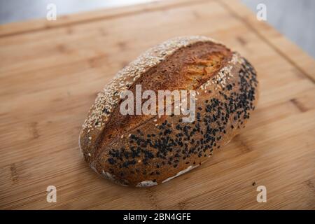 Craft Bread wird mit weißen und schwarzen Sesamsamen auf einem Holzhintergrund mit Kopierraum bestreut Stockfoto