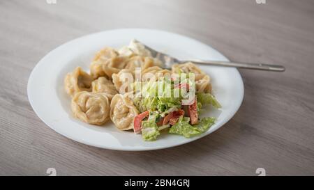 Knödel mit Gemüsesalat auf einem weißen Teller und einem Holztisch Stockfoto
