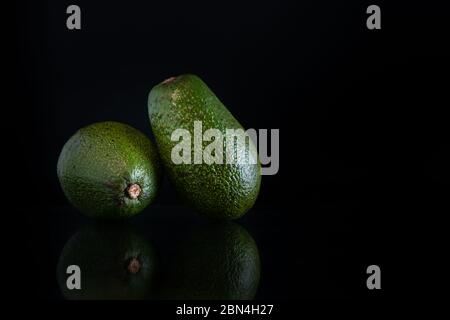 Zwei ganze Avocados mit Spiegelung und Kopierraum auf schwarzem Hintergrund Stockfoto
