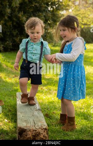 Ältere Schwester hilft jüngeren Bruder Gleichgewicht entlang log Stockfoto