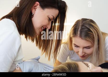 Zwei fröhliche selbstbewusste Kosmetologen tun Haarentfernung. Zwei glückliche Frauen machen das Achseldepilationsverfahren. Das Konzept der Lehre depilation Stockfoto