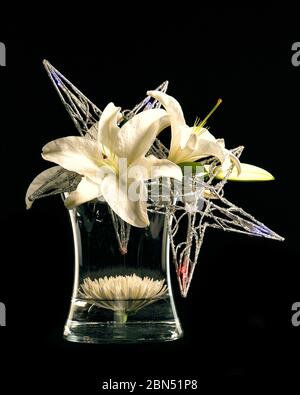 Ein florales Arrangement aus Sternengucker-Lilien und glitzernden Accessoires auf schwarzem Hintergrund. Stockfoto