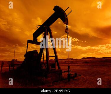 Ein Ölfeld-Pumpenheber, der bei Sonnenuntergang Öl aus dem Boden pumpt. Stockfoto