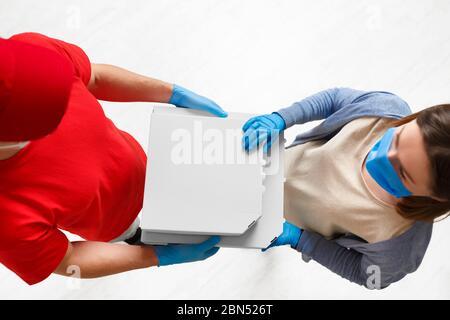 Sterile Lieferung von Pizza. Kurier und Kunde in medizinischen Masken und Handschuhen Stockfoto