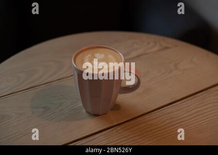 Eine Tasse heißen Cappuccino auf einem Holztisch. Cappuccino mit Latte Art in einer schönen Tasse auf dem Tisch in einem Café. Selektiver Fokus. Zu Hause. Zeit fo Stockfoto