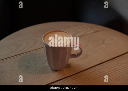 Eine Tasse heißen Cappuccino auf einem Holztisch. Cappuccino mit Latte Art in einer schönen Tasse auf dem Tisch in einem Café. Selektiver Fokus. Zu Hause. Zeit fo Stockfoto