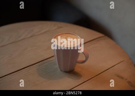 Eine Tasse heißen Cappuccino auf einem Holztisch. Cappuccino mit Latte Art in einer schönen Tasse auf dem Tisch in einem Café. Selektiver Fokus. Zu Hause. Zeit fo Stockfoto