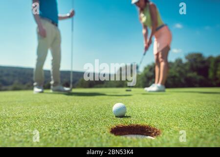 Paar Golf spielen mit der Frau auf grün zu Loch in Stockfoto