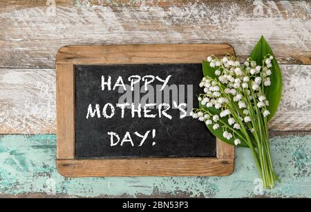 Maiglöckchen Blumen mit Kreidetafel auf rustikalem Holzhintergrund. Alles Gute Zum Muttertag Stockfoto