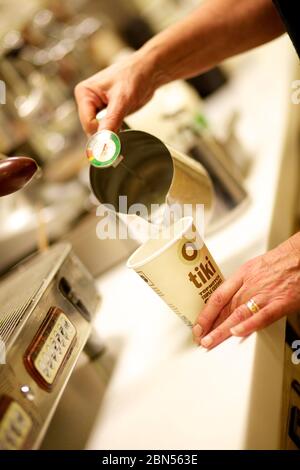 Kaffee wird in eine Take-out-Tasse mit der Kaffeemaschine im Hintergrund gegossen, Stockfoto
