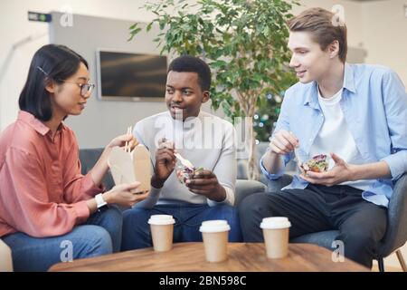 Multiethnische Gruppe junger Menschen, die Essen zum Mitnehmen essen und während der Mittagspause im Büro plaudern Stockfoto