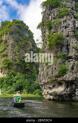 Menschen in traditionellen vietnamesischen Hüte im Boot entlang des Flusses. Pass in der Nähe von schönen Klippen. Traditionelle vietnamesische Boot mit Ruder. Ruderboot Tam Coc Tour Stockfoto