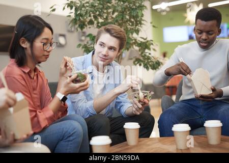 Multiethnische Gruppe von Teenagern, die Essen zum Mitnehmen essen und während der Mittagspause im College plaudern Stockfoto