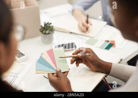 Nahaufnahme eines nicht erkennbaren afroamerikanischen Mannes, der Farbfelder hält, während er mit Kollegen während des Treffens im Büro ein Designprojekt diskutiert, Kopie Stockfoto