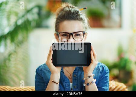 Glücklich stilvolle 40 Jahre alte Hausfrau in Jeans-Shirt bei modernen Hause in sonnigen Tag versteckt hinter Tablet-PC leeren Bildschirm. Stockfoto