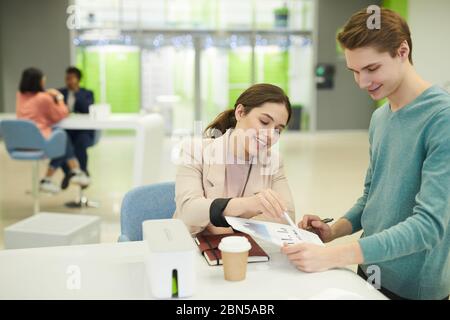 Porträt zweier fröhlicher Studenten, die während der Mittagspause im College am Tisch über das Studienprojekt diskutieren Stockfoto