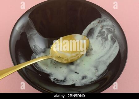 Reste von geschmolzenem Minze Eis nach dem Abschluss der Mahlzeit in schwarzer Schüssel mit goldenem Löffel auf rosa Hintergrund Stockfoto