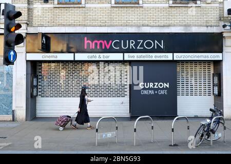 Eine Frau in einer Gesichtsmaske geht am HMV Curzon Cinema in Wimbledon vorbei, das derzeit während der Coronavirus-Pandemie als nicht-essentielles Geschäft geschlossen wird. Stockfoto