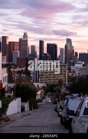 Blick auf eine hügelige Wohnstraße in Los Angeles bei Sonnenuntergang mit Blick auf die Innenstadt VON LA