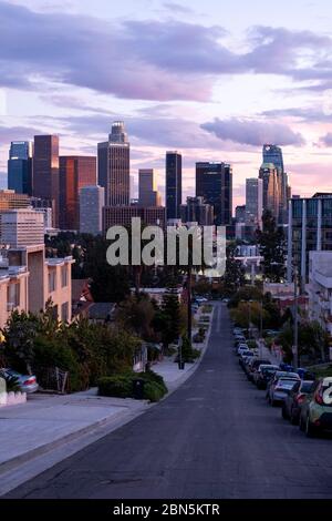 Blick auf eine hügelige Wohnstraße in Los Angeles bei Sonnenuntergang mit Blick auf die Innenstadt VON LA