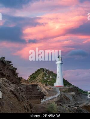 Leuchtturm im Abendlicht unter einem rosa bewölkten Himmel auf den Klippen von Castlepoint, Lavafels, Masterton, Wellington, Neuseeland Stockfoto