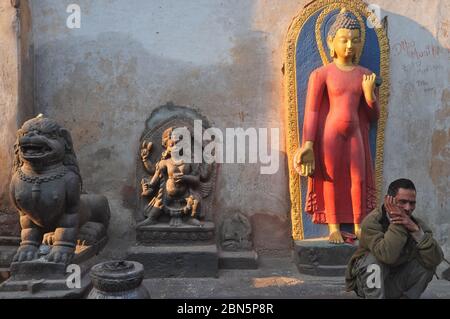 Auf dem Gelände des swayambhunath Temple, Kathmandu, Nepal, sitzt ein Mann neben einer Buddha-Statue, einer Statue des Hindu-gottes Bhairav und einer Löwenwächter-Statue Stockfoto