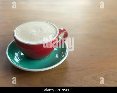 Eine Tasse Cappuccino, raf-Kaffee, auf Holzgrund. Roter Keramikbecher und grüner Untertopf. Stockfoto