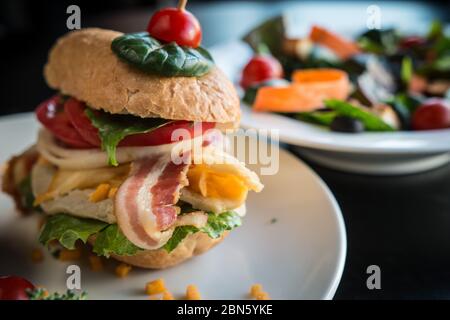 Nahaufnahme eines geladenen Burgers mit Baguette Patty und einem Teller Salat. Stockfoto